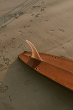 Close-up of hands shaping a surfboard, surrounded by sand and ocean spray.