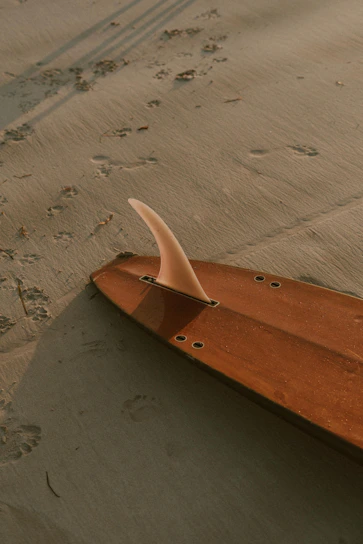 A sleek surfboard made from reclaimed wood and old board parts, resting on the sand at sunset.