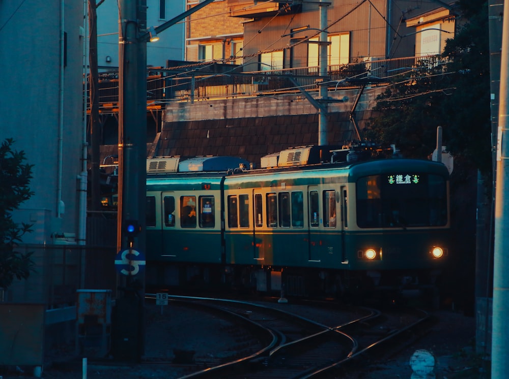 a green train traveling down train tracks next to a tall building