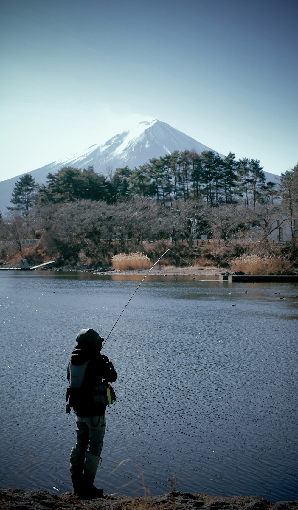 a man fishing on a lake with a mountain in the background