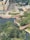 Aerial view of an urban area that includes a large building complex, pathways, roads, and a partially visible water feature surrounded by trees. A construction site with machinery and a crane can also be seen, alongside a park area with lush greenery.