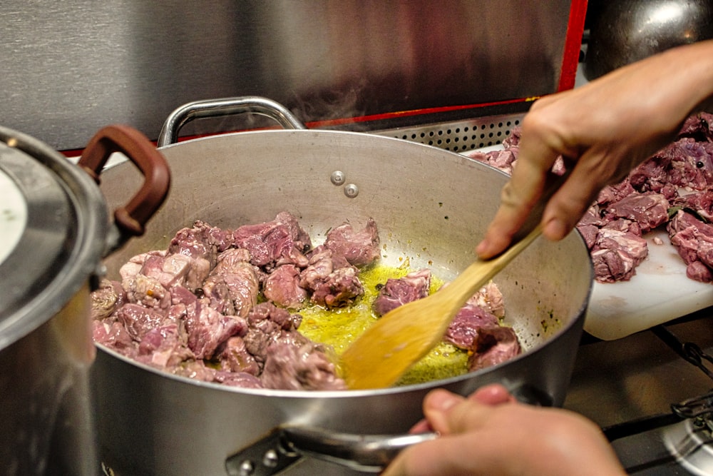 una persona cocinando carne en una olla en la estufa