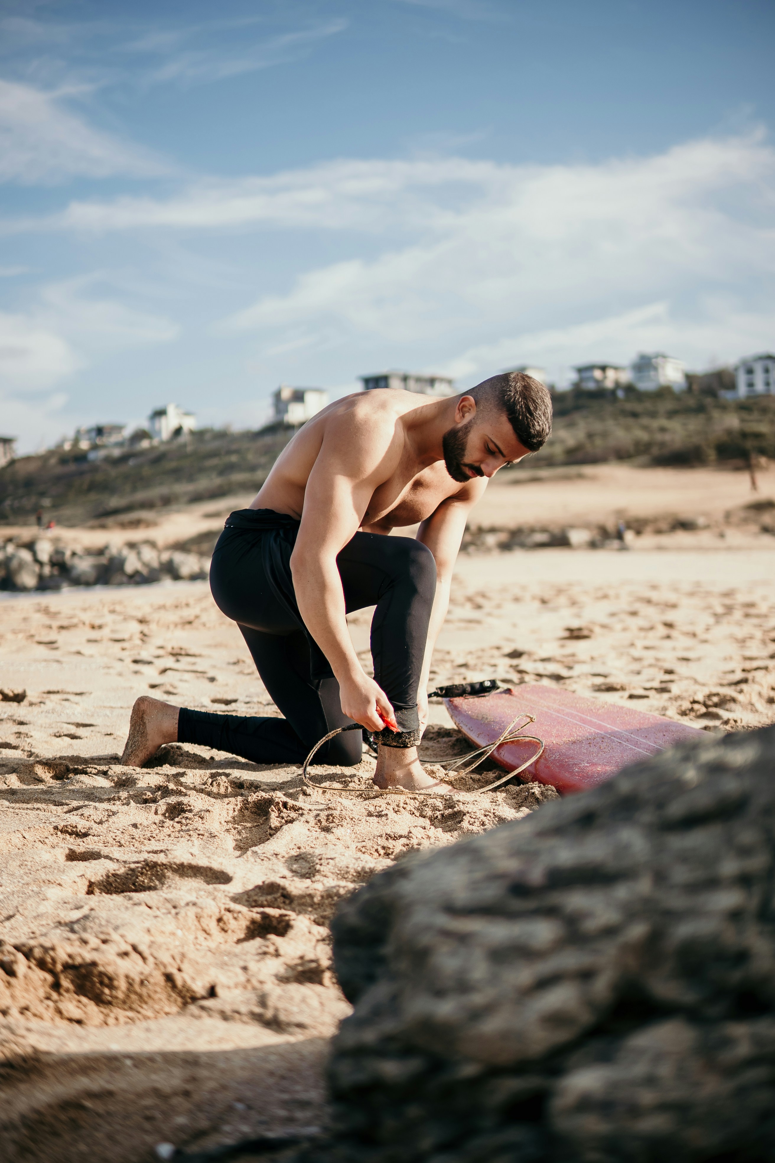 a man kneeling down on a beach next to a surfboard