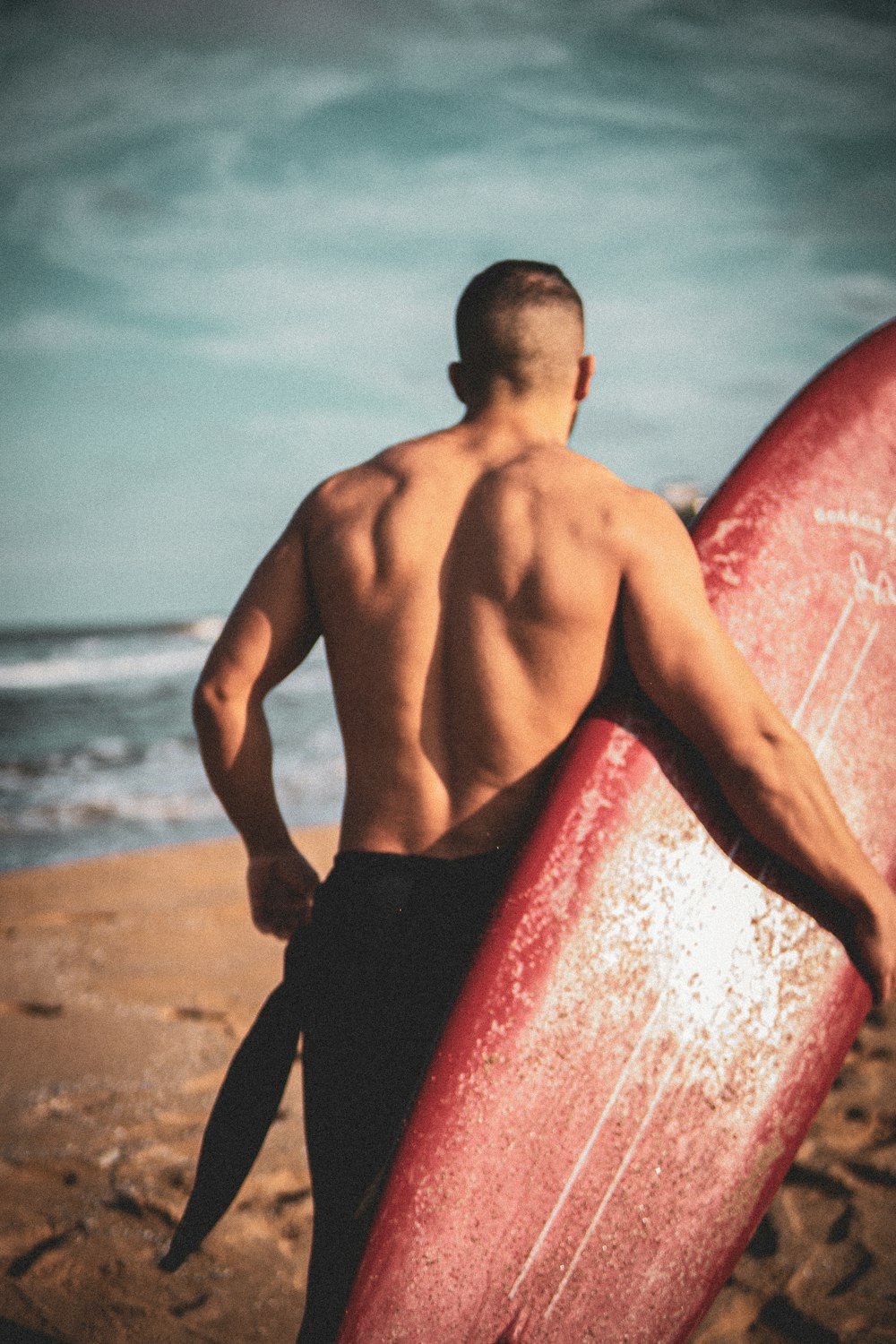 a man holding a red surfboard on a beach