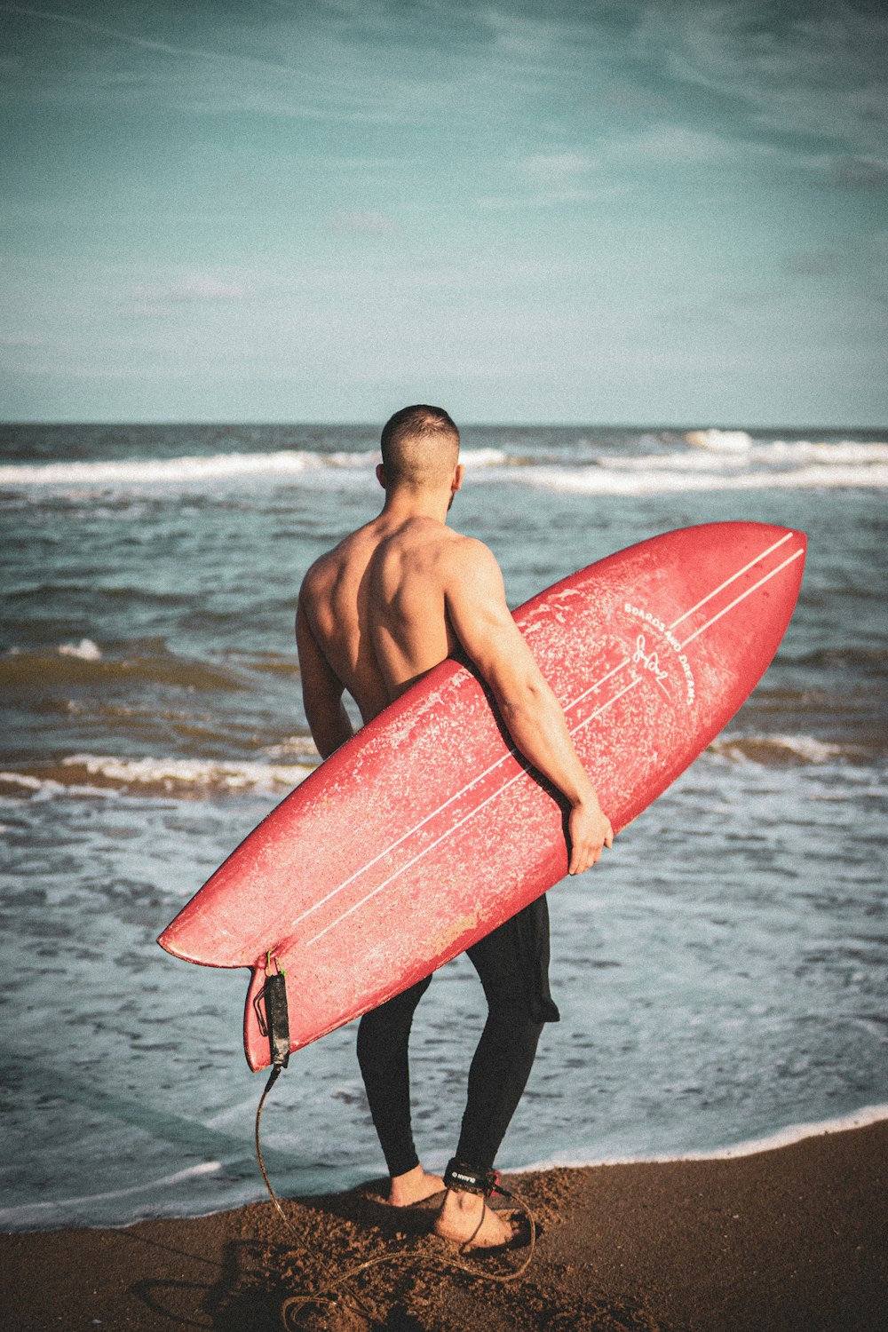 a man holding a red surfboard on top of a beach