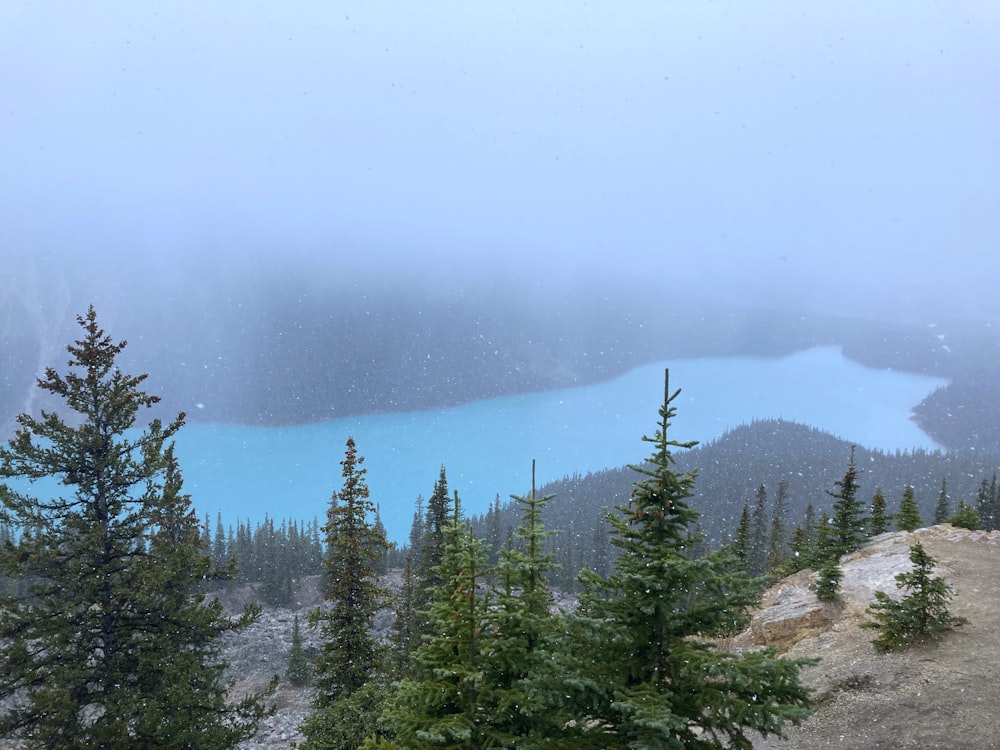 a blue lake surrounded by trees on a foggy day