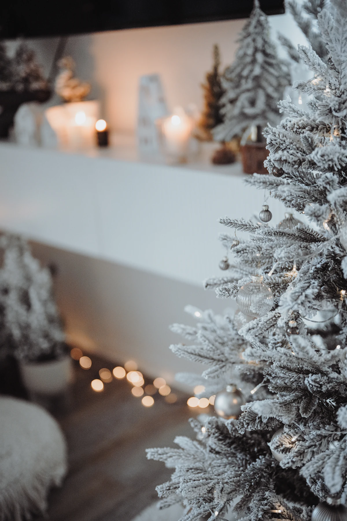 A white, snow-look Christmas tree in front of a fireplace