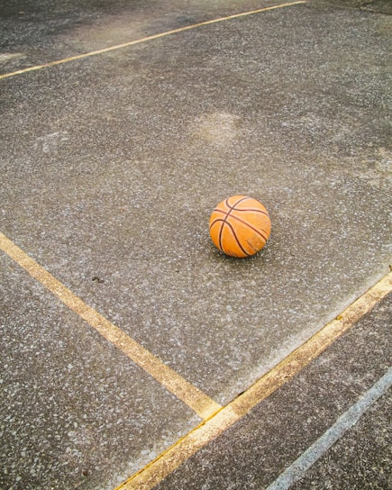 A close-up shot of a well-used basketball resting on an outdoor cement court bathed in golden afternoon light.