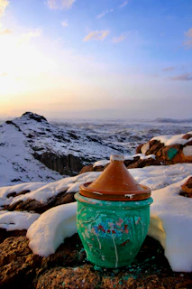 Traditional Kashmiri matka dahi set on a green meadow with snow-capped mountains in the background.