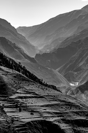 A black and white photo of a narrow mountain path winding through terraced fields under a cloudy sky.