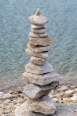 Close-up of smooth river stones stacked in a balanced tower on a sandy shore.