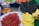 A vibrant display of various fruits including bananas, red cherries, peaches, green grapes, and mulberries arranged on market tables. The cherries are piled high in a large mound, bananas are neatly stacked in clusters, and the mulberries are individually packaged in small containers.