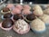 An assortment of round, chocolate-colored treats placed in colorful, decorative paper cups on a speckled gray tray. The sweets vary in texture, some dusted with cocoa or covered in shredded coconut and other ingredients.