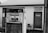 A vintage gas pump is positioned in front of a modest building with a sign indicating 'Pinecrest Service Station' and a note on the door reading 'Closed Gone Fishin'. The pump shows wear and age, with faded numerals and a rustic surface. A simple chair is also visible near the door.