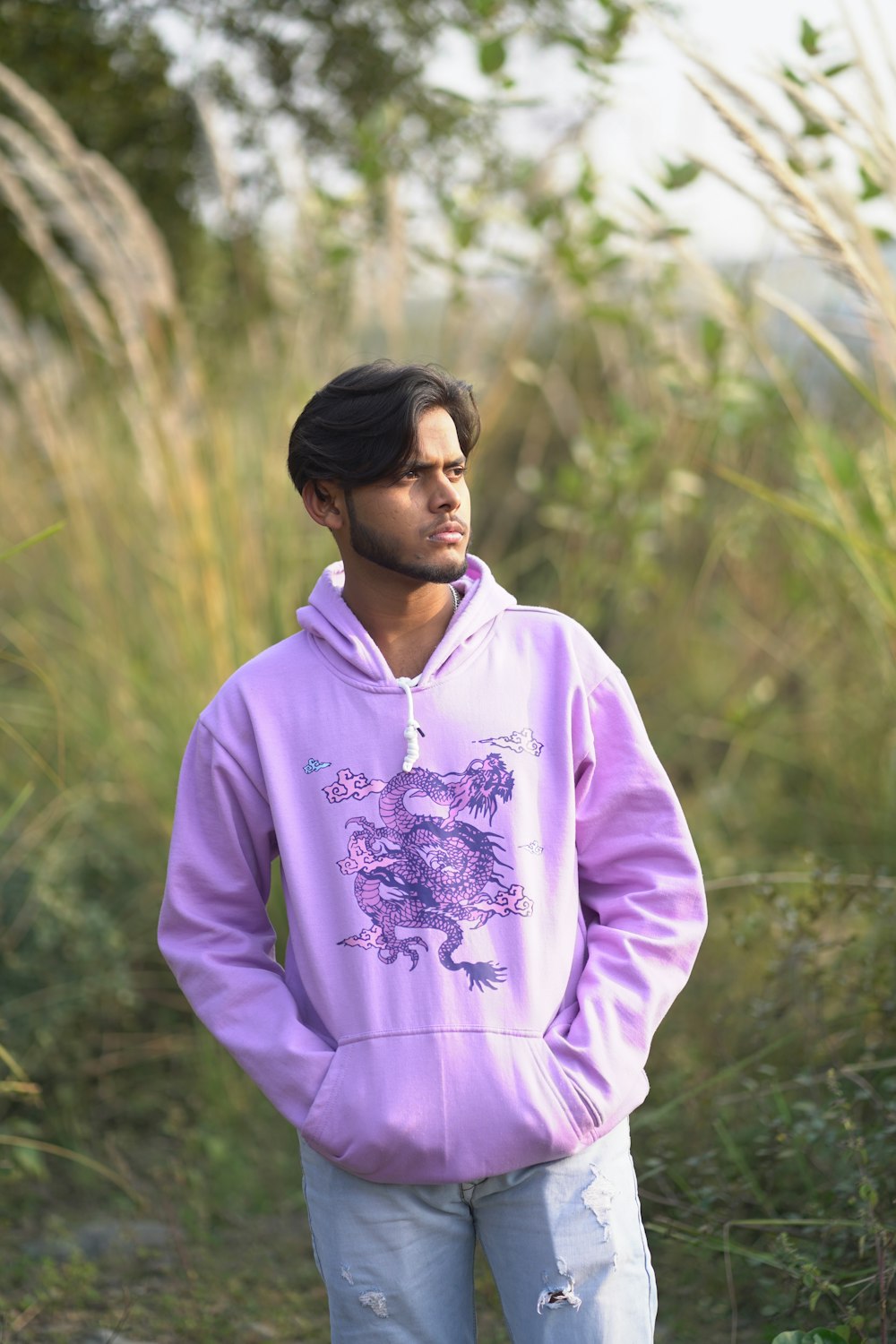 a man standing in a field wearing a purple hoodie