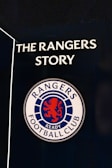 A sign featuring the words 'The Rangers Story' above a round emblem with a red lion and the words 'Rangers Football Club.'