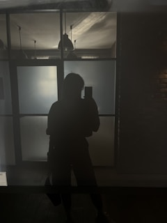 A silhouette of a person holding a phone standing in front of frosted glass panels with hanging pendant lights and a brick wall in the background.