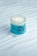 A jar of hair mask with a creamy white substance is displayed on a textured surface. The packaging features a blue label with the brand name 'VITA COCO' and illustrated green leaves.