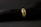A gold ring adorned with various gemstones is displayed against a soft, black textured background. The gemstones include red, blue, and transparent stones, each embedded in the band, adding vibrant colors to the ring's elegant design.