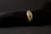 A gold ring adorned with various gemstones is displayed against a soft, black textured background. The gemstones include red, blue, and transparent stones, each embedded in the band, adding vibrant colors to the ring's elegant design.