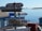 Several directional signs are pointing towards various locations such as Palmer Station, McMurdo, Scott Station Base, South Pole, Ward, and Punta Arenas. The signs indicate the distances in miles to these places. In the background, there is a view of an icy landscape with calm water and icebergs, under a clear blue sky.