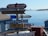 Several directional signs are pointing towards various locations such as Palmer Station, McMurdo, Scott Station Base, South Pole, Ward, and Punta Arenas. The signs indicate the distances in miles to these places. In the background, there is a view of an icy landscape with calm water and icebergs, under a clear blue sky.