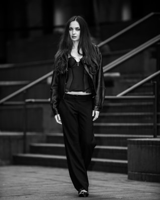 Monochrome photo of a model walking through a dimly lit alley wearing layered noirenaire apparel.