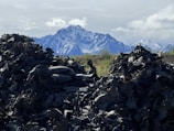 Mounds of discarded tires dominate the foreground, creating a stark contrast against the distant snow-capped mountains. The sky is partly cloudy with patches of blue visible.