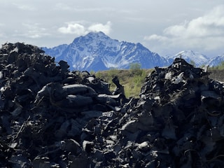 Mounds of discarded tires dominate the foreground, creating a stark contrast against the distant snow-capped mountains. The sky is partly cloudy with patches of blue visible.