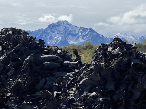 Mounds of discarded tires dominate the foreground, creating a stark contrast against the distant snow-capped mountains. The sky is partly cloudy with patches of blue visible.