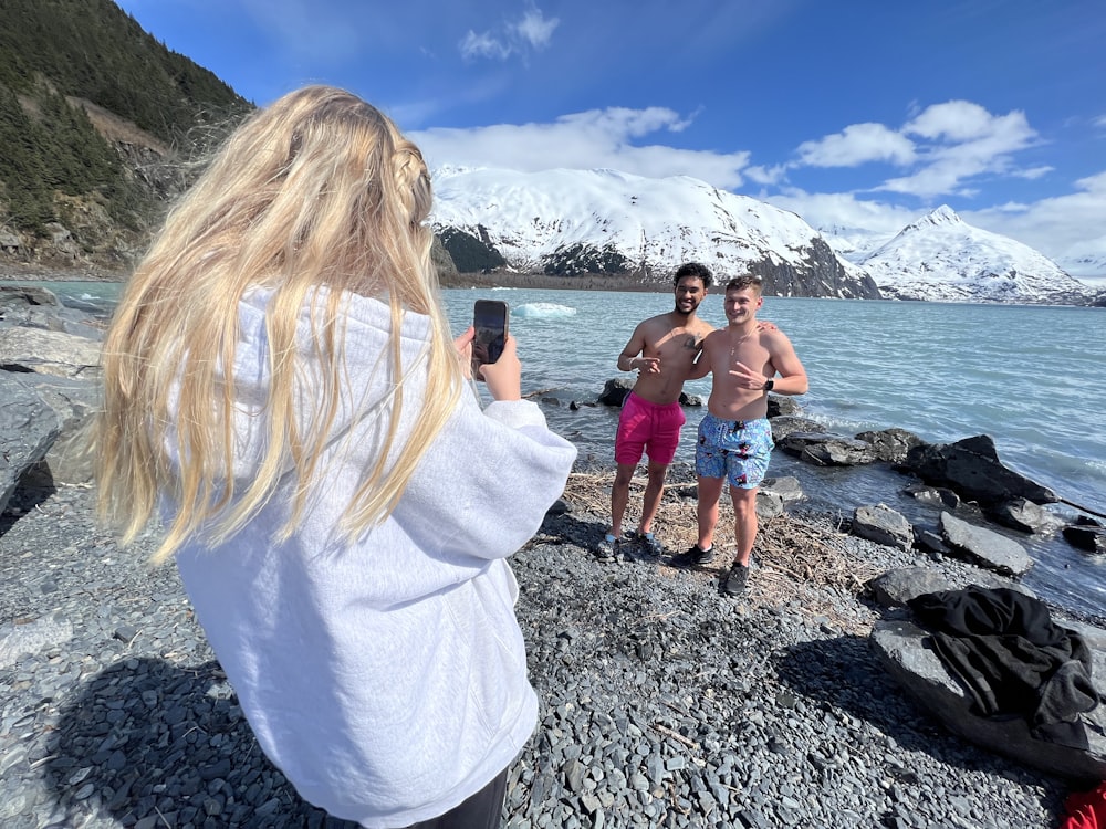 a woman taking a picture of two men on the beach