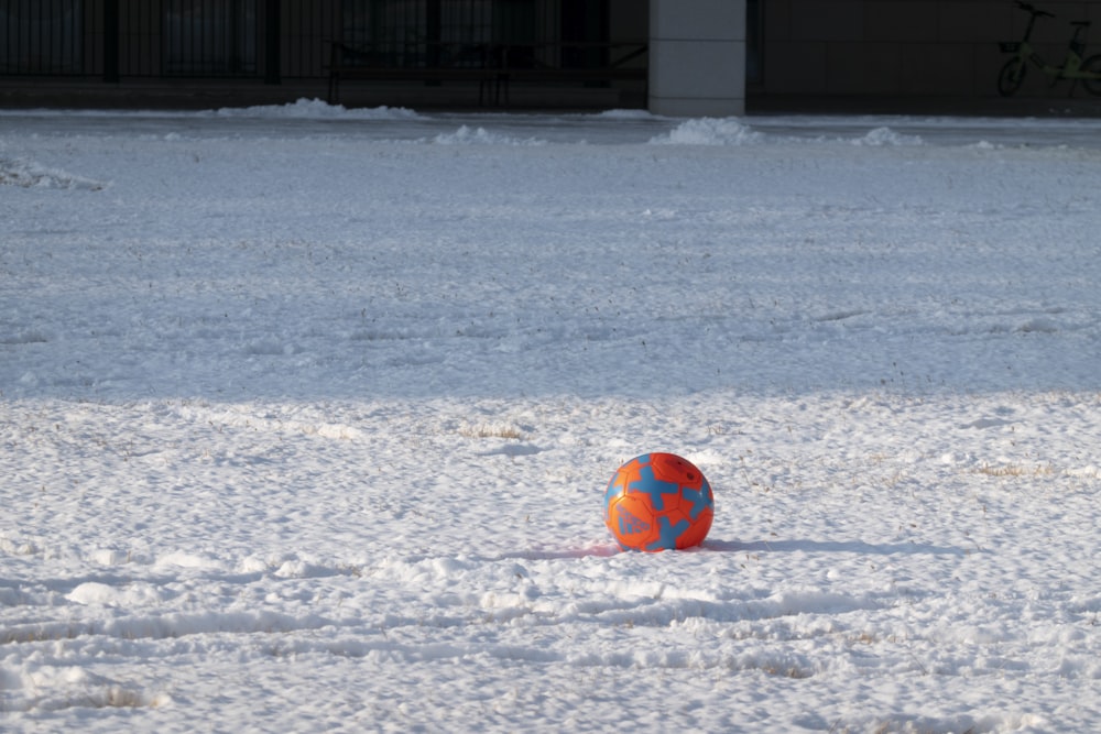 an orange and blue ball sitting in the snow