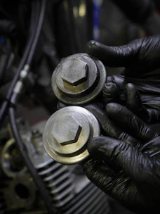 Worker's hands holding a handful of shiny screws in a gritty factory setting.