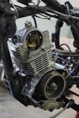 A detailed view of a partially disassembled motorcycle engine is surrounded by various metal parts and wires.