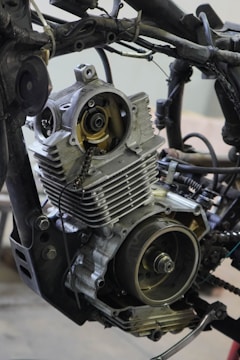 A detailed view of a partially disassembled motorcycle engine is surrounded by various metal parts and wires.
