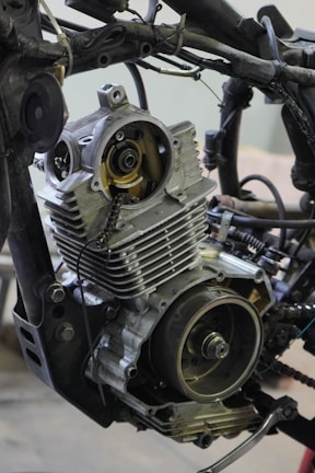 A detailed view of a partially disassembled motorcycle engine is surrounded by various metal parts and wires.