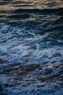 Soft ocean waves with white foam rolling onto a sandy beach at golden hour.