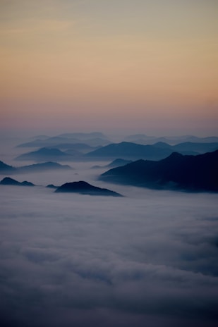 A serene mountain range at dawn with soft pastel skies and gentle mist.
