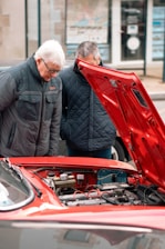 two men looking under the hood of a red car