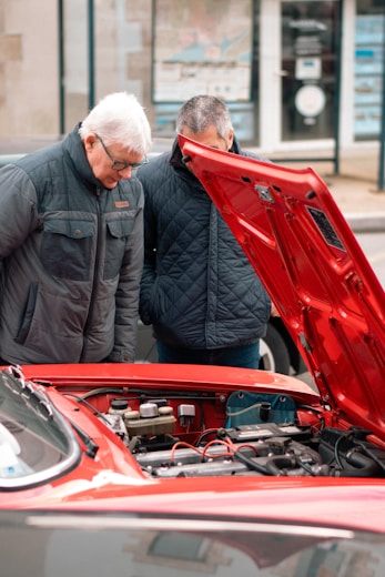 two men looking under the hood of a red car