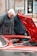 two men looking under the hood of a red car