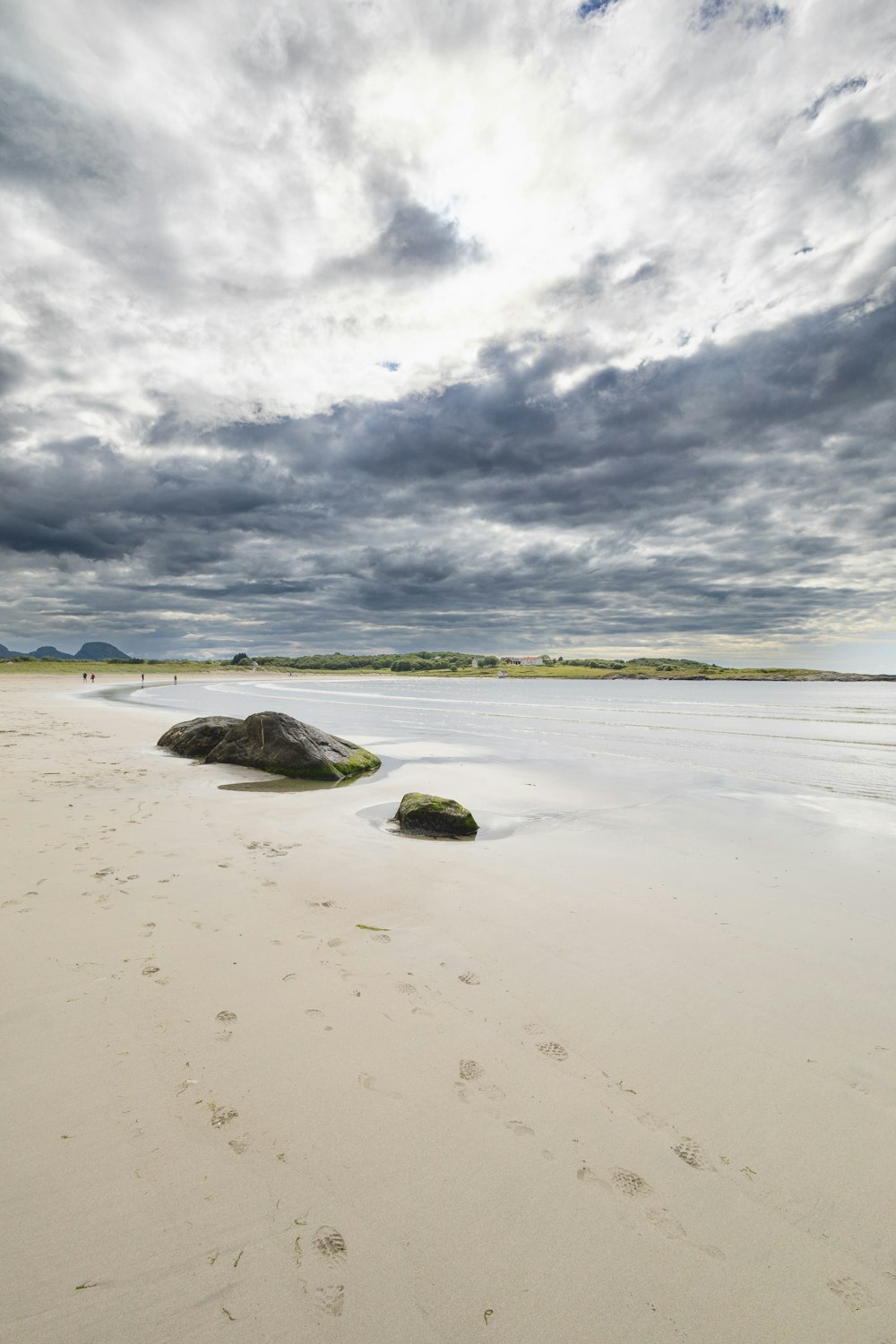 a sandy beach with rocks and water under a cloudy sky