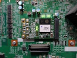 A printed circuit board with various electronic components and integrated circuits, prominently featuring a large black chip labeled 'PHOENIX ICU PRG 0770Z1-1'. Several capacitors are visible, along with numerous small resistors and connectors. There is a green LED light illuminated on the board, and the surface is covered with intricate traces and solder points.