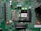 A printed circuit board with various electronic components and integrated circuits, prominently featuring a large black chip labeled 'PHOENIX ICU PRG 0770Z1-1'. Several capacitors are visible, along with numerous small resistors and connectors. There is a green LED light illuminated on the board, and the surface is covered with intricate traces and solder points.