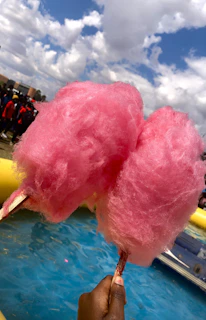 Smiling children enjoying fluffy pink cotton candy under bright festival lights.