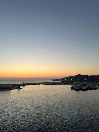A serene harbor at sunset with calm waters and soft glowing lights reflecting on the surface.