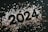 The image features black numerals forming the year 2024 surrounded by scattered star-shaped confetti. The confetti varies in color, including shades of silver and gold, creating a celebratory atmosphere.