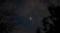 A mystical night sky with a crescent moon shining over a silhouette of a woman in spiritual meditation.