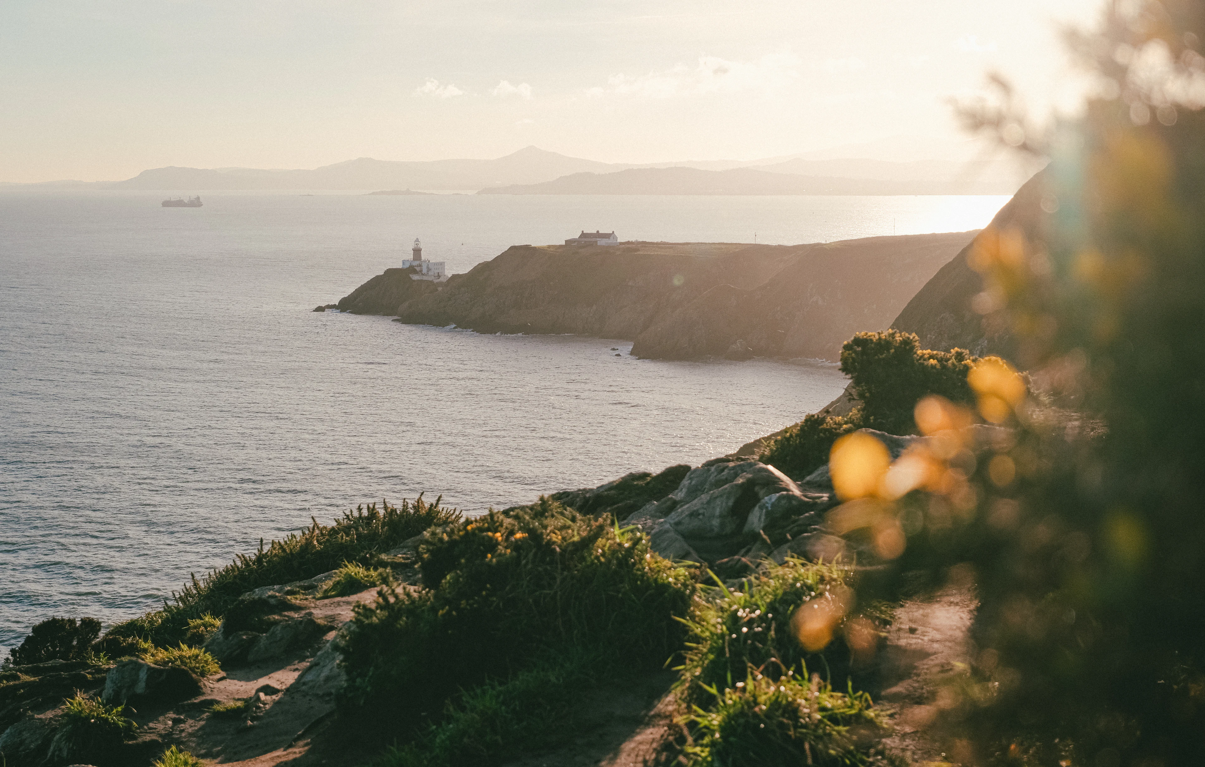 Cliffs and a lighthouse point on Howth Head seen across the sea in golden evening light.