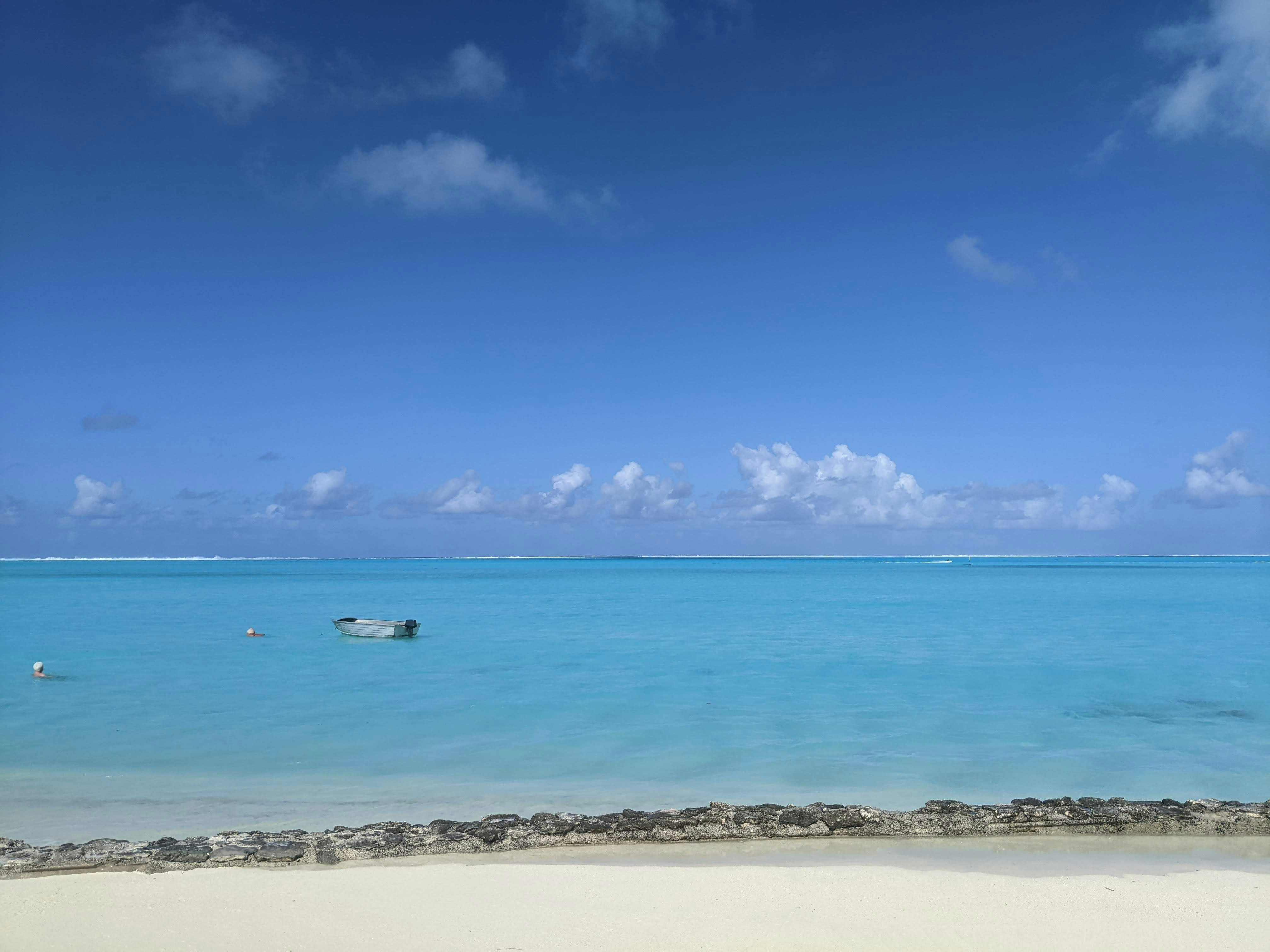 a boat floating on top of a blue ocean next to a sandy beach, 